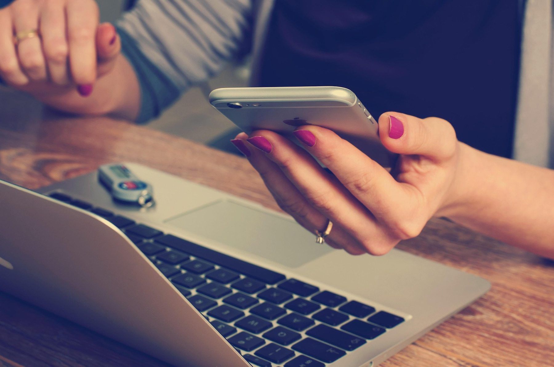 Person using a smartphone while working on a laptop at a desk